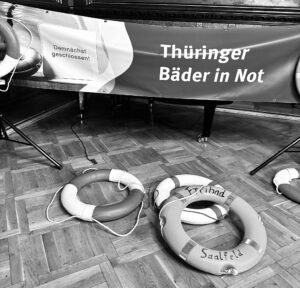 Ein schwarz-weißes Foto von Rettungsreifen. Auf dem Banner steht "Thüringer Bäder in Not"